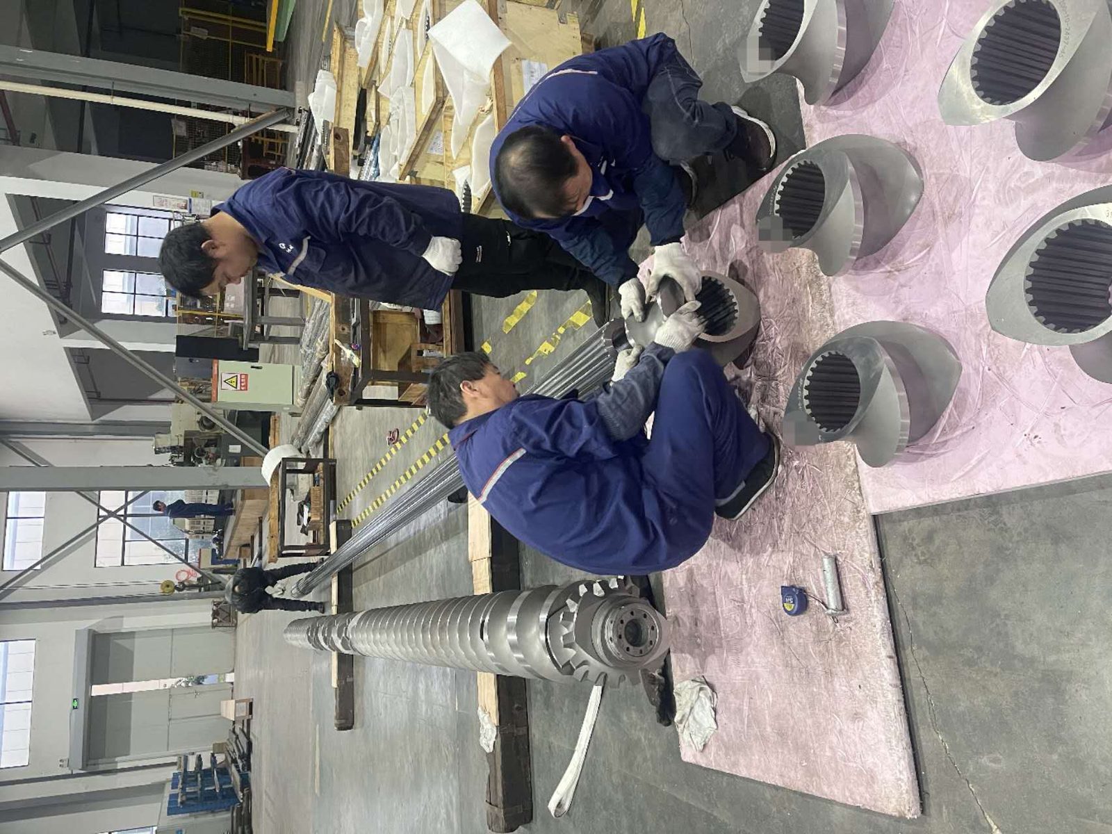 Technicians assembling large twin-screw extruder elements in workshop